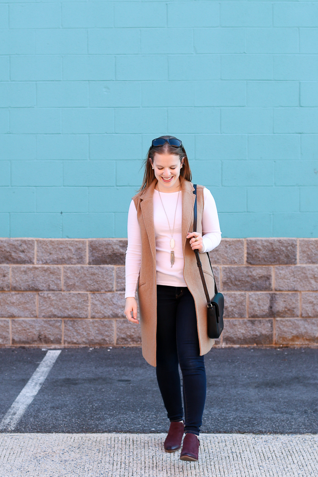 woman in long sweater, pink top, and jeans for Cute Thanksgiving Outfit Ideas